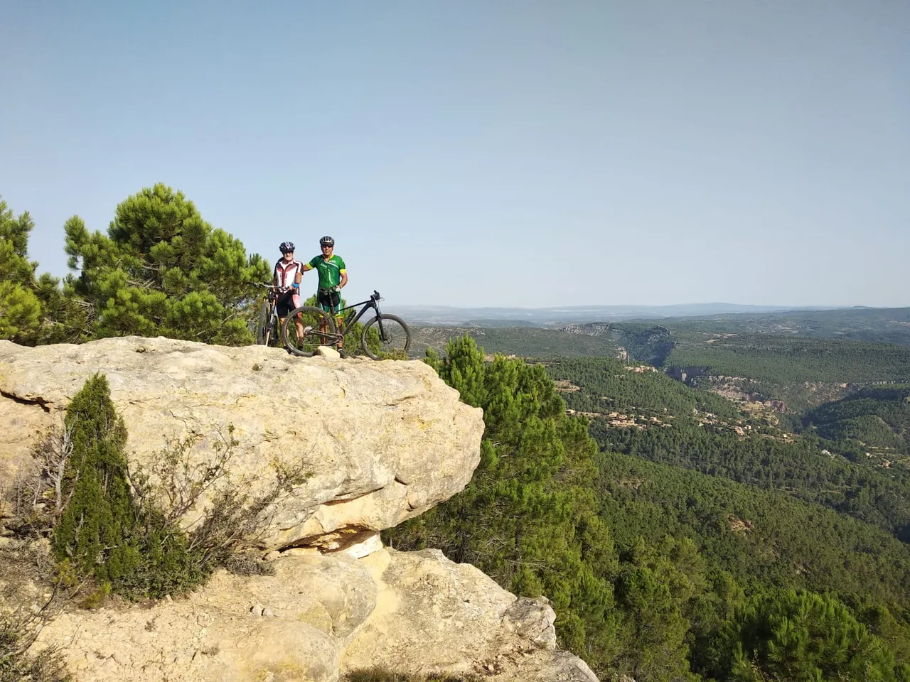Dos ciclistas asomados a una peña voladiza sobre el pinar