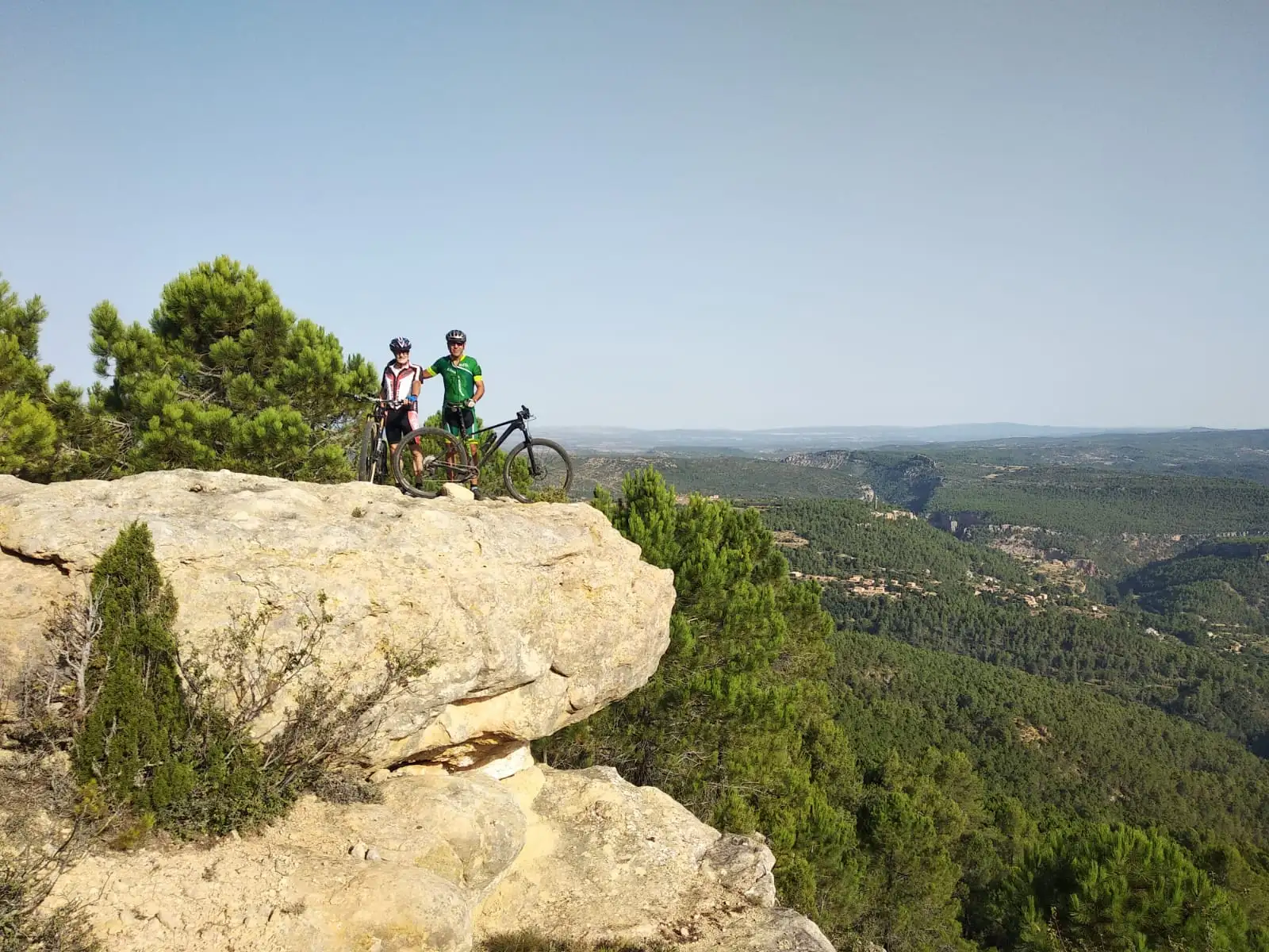 Dos ciclistas asomados a una peña voladiza sobre el pinar