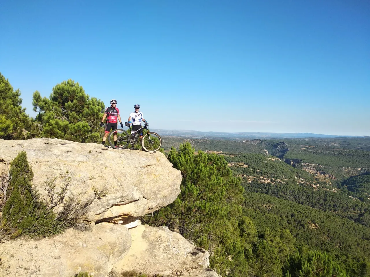 Dos ciclistas en una roca voladiza con panorámica amplia