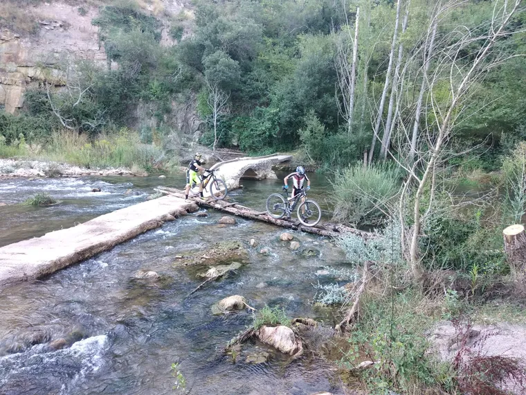 Dos ciclistas cruzando el puente de troncos sobre el río