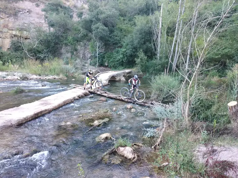 Dos ciclistas cruzando el puente de troncos sobre el río