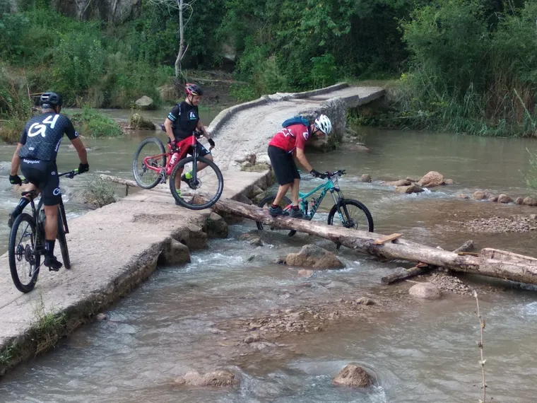 Tres ciclistas cruzando el azud y la pasarela a la vez