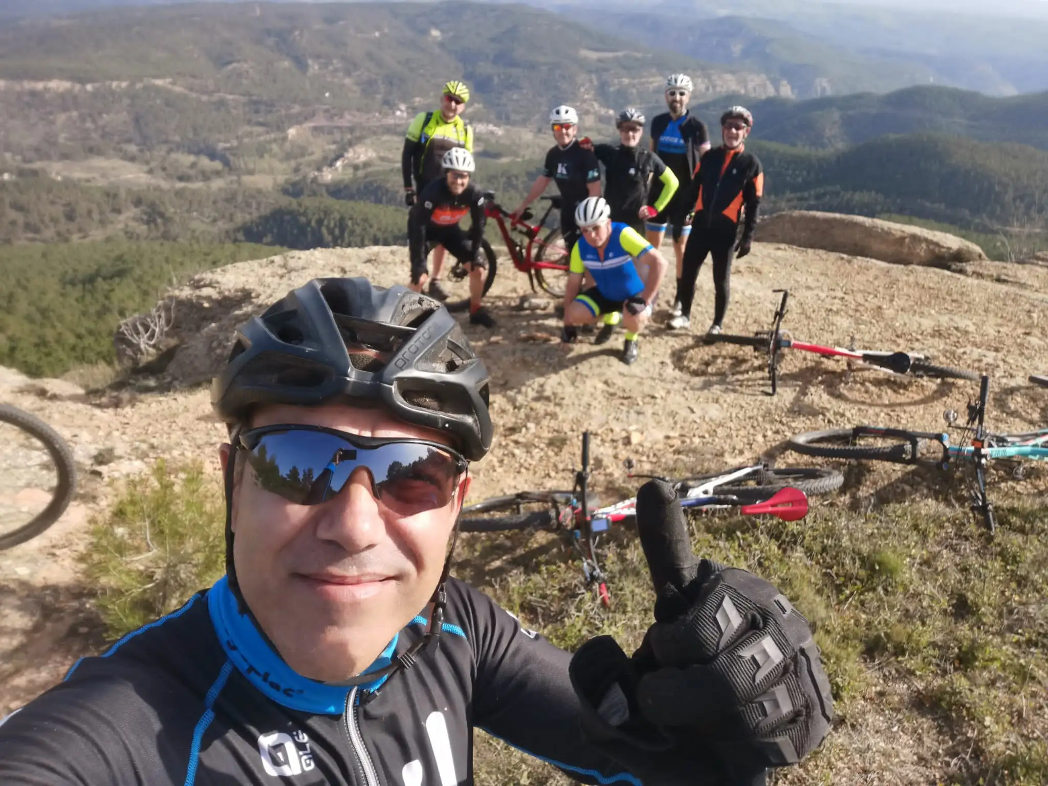 Selfie de todo el grupo en la cima, con las bicis tumbadas y el mar de montes detrás