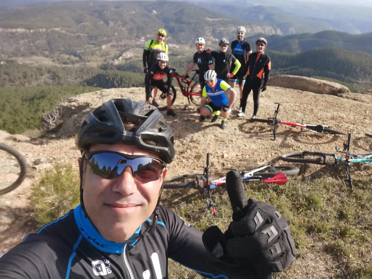 Selfie de todo el grupo en la cima, con las bicis tumbadas y el mar de montes detrás