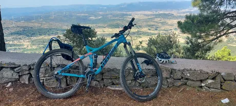 Una MTB apoyada en un muro de piedra seca con el valle y los aerogeneradores detrás
