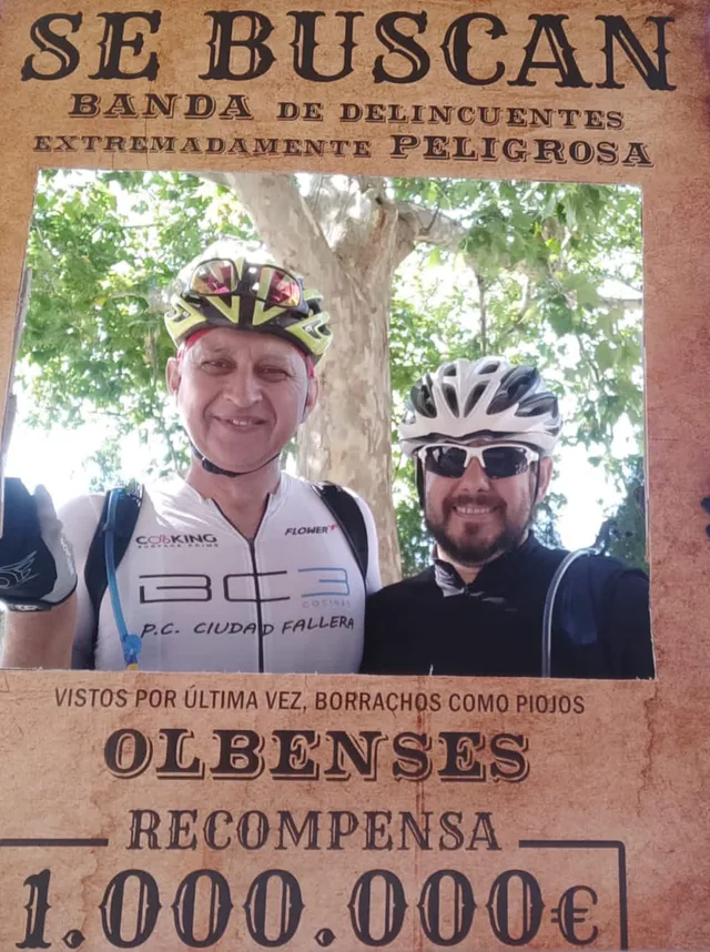 Dos ciclistas asomados al hueco de un photocall con forma de cartel del oeste: se buscan, banda de delincuentes extremadamente peligrosa, olbenses, vistos por última vez borrachos como piojos, recompensa un millón de euros