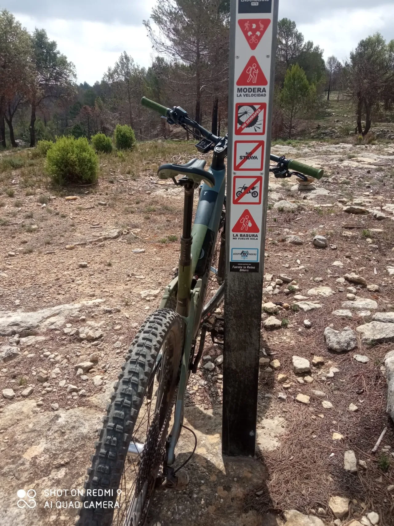 Una MTB verde apoyada en el poste del sendero adoptado