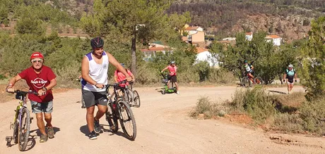 El grupo de la marcha empujando las bicis con el pueblo y las montañas al fondo