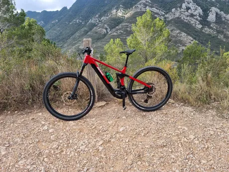 Una e-bike roja apoyada en un poste, esperando