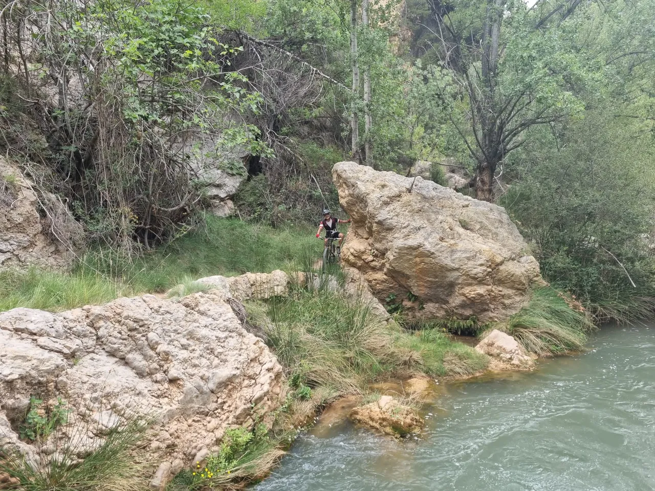 Ciclista junto a una roca gigante y el agua turquesa del Mijares