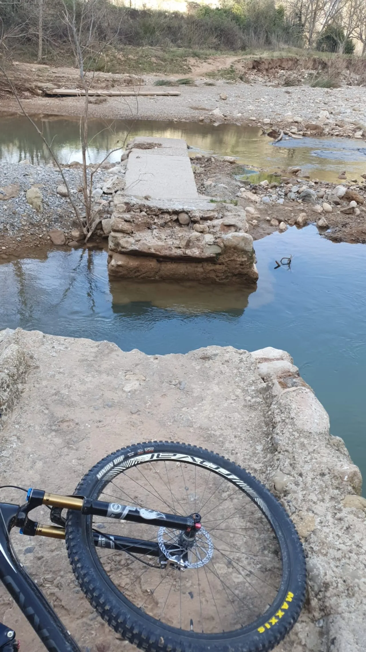 Una rueda de MTB en primer plano ante el vado del río