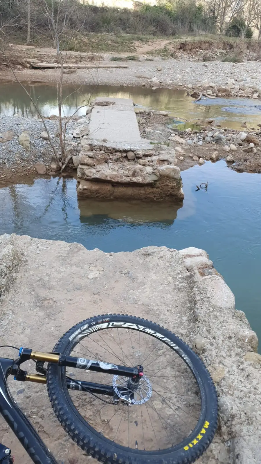 Una rueda de MTB en primer plano ante el vado del río
