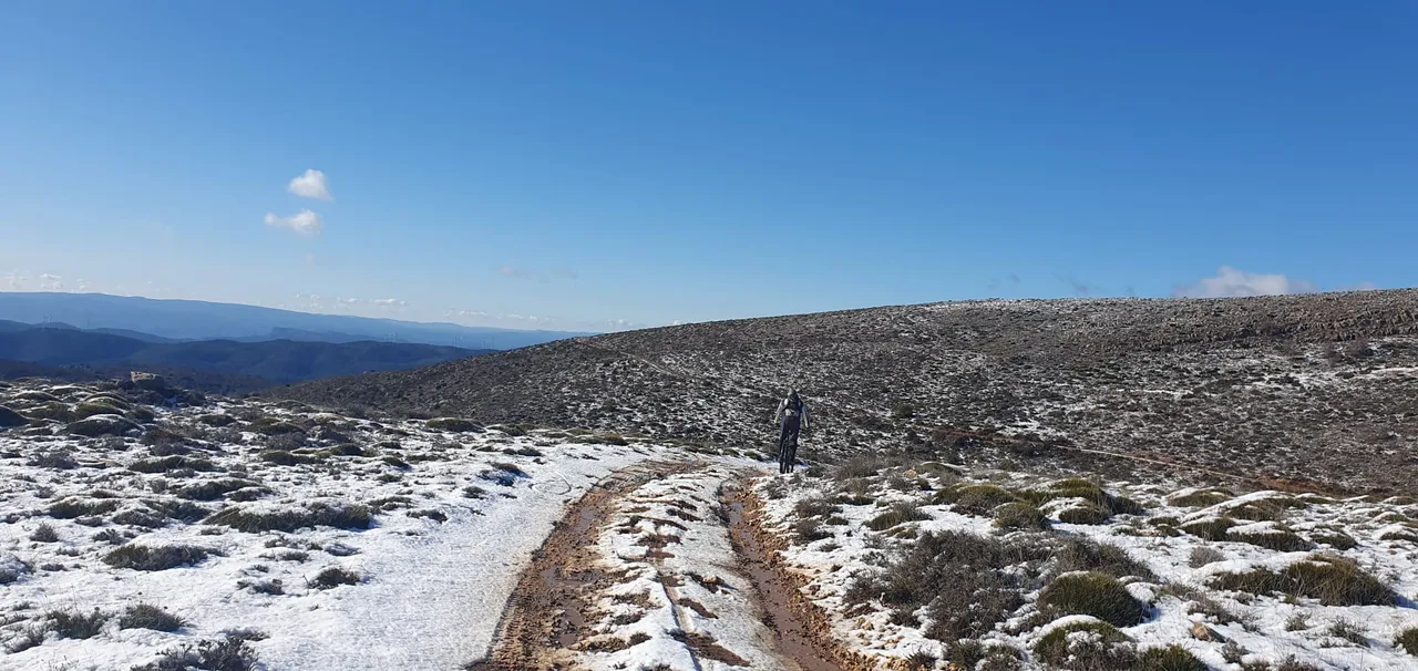 Ciclista solitario en una loma nevada con las sierras al fondo