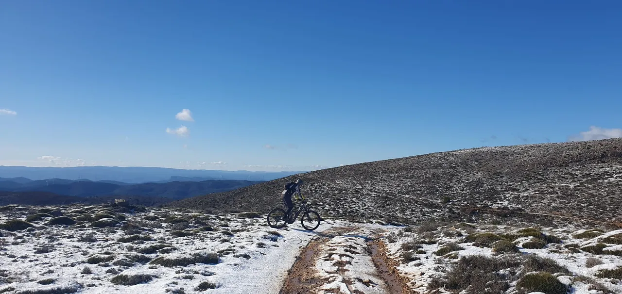 Ciclista en una meseta nevada con horizonte infinito de sierras