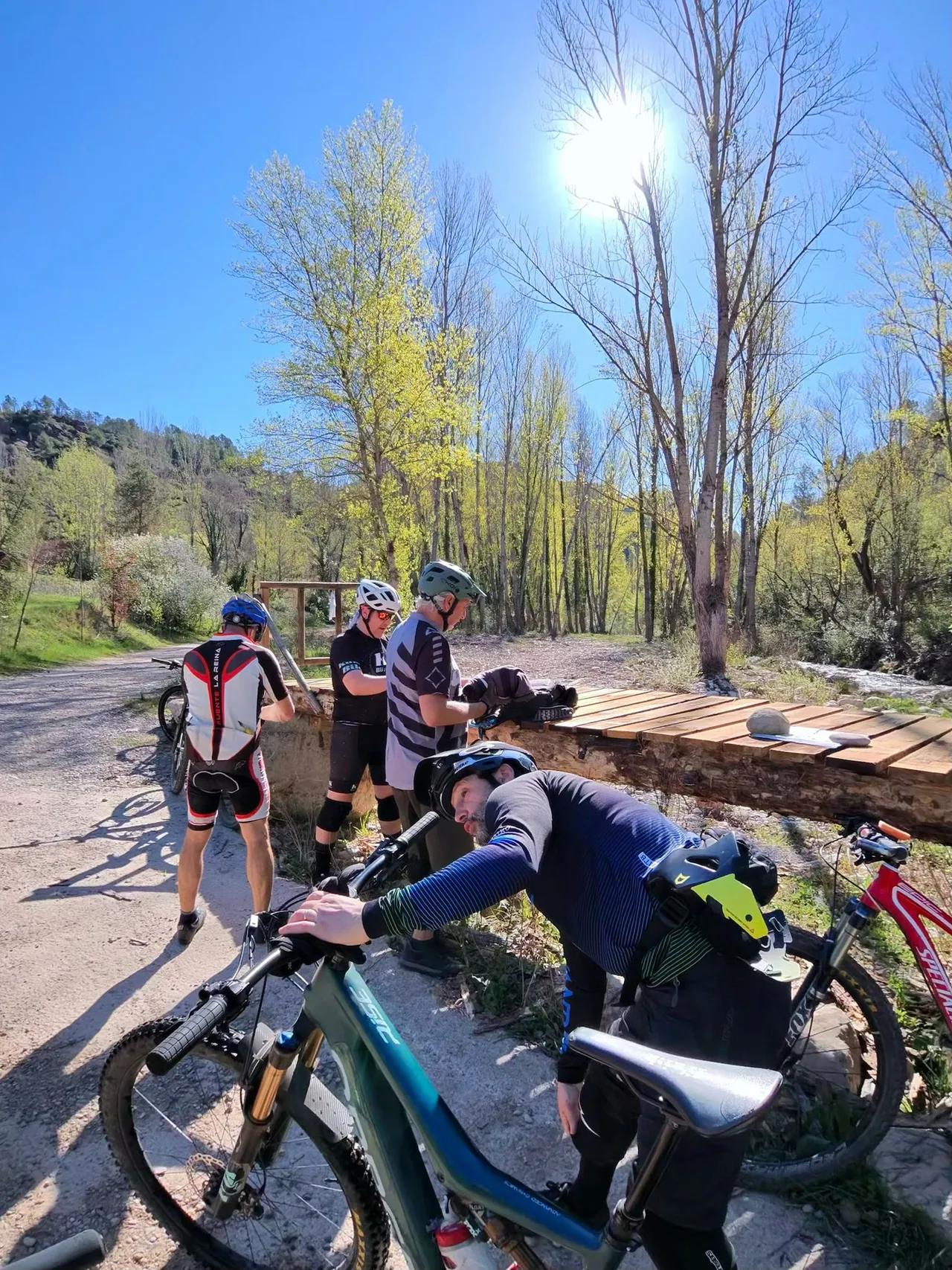 El grupo parado junto a la pasarela de madera nueva sobre el río, entre chopos de primavera