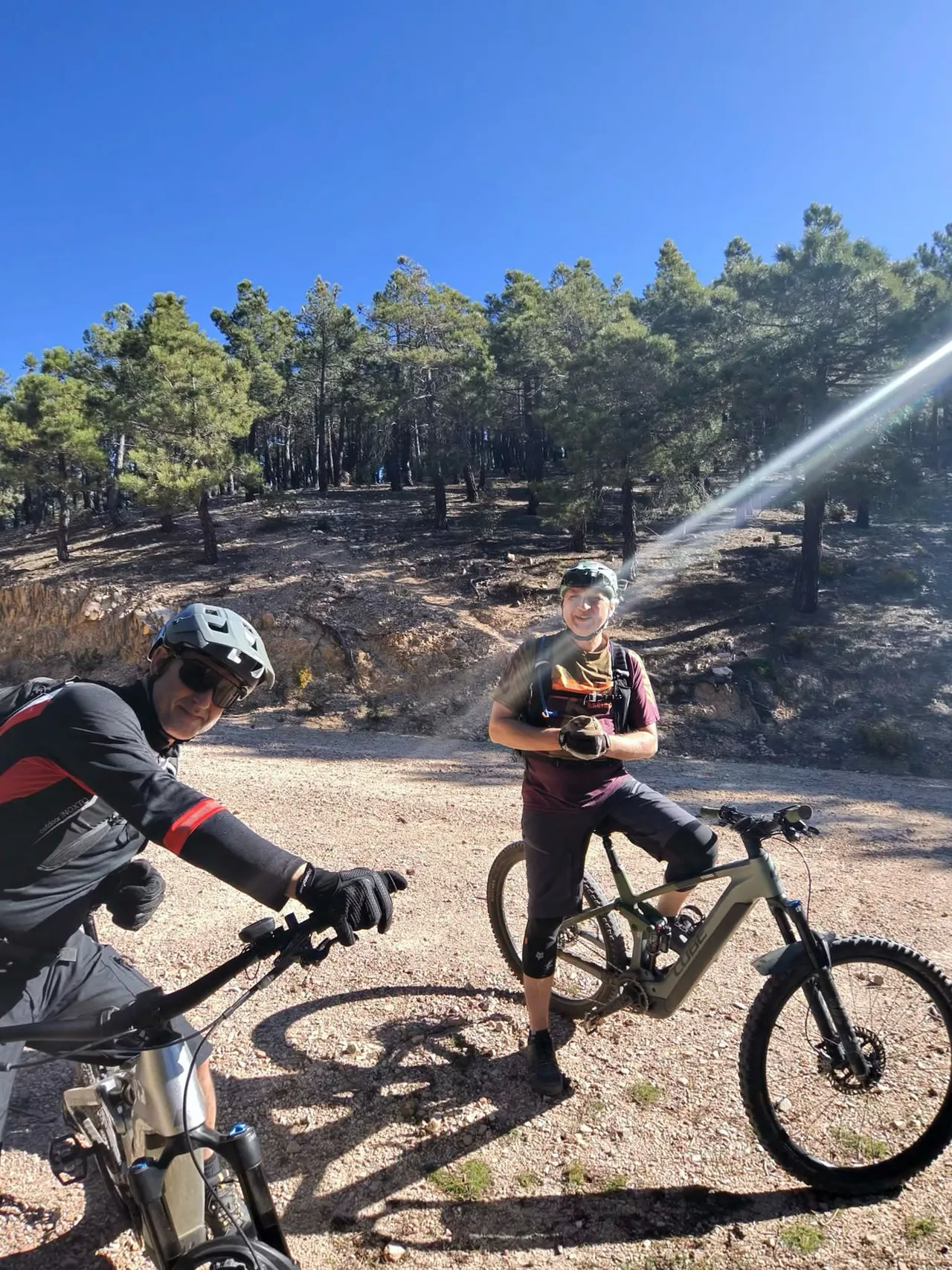 Dos bikers con las e-bikes en la pista del pinar, con el sol de cara